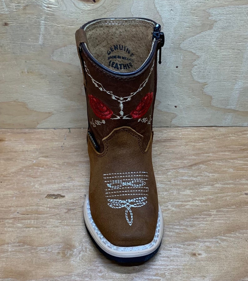 May include: Brown leather children's cowboy boots with red embroidered roses and a zipper on the side. The boots have a white sole and say "Genuine Leather Made in Mexico" on the inside.