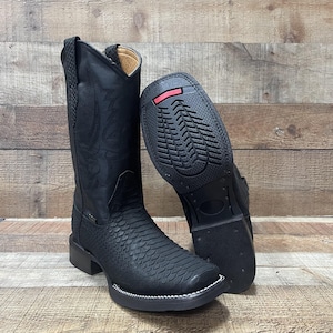 May include: Black leather cowboy boots with a square toe and decorative stitching. The boots have a textured pattern on the vamp and a contrasting white stitch around the sole. The sole is black with a red accent.