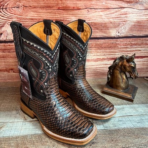 May include: A pair of brown leather cowboy boots with intricate embroidery and a snakeskin pattern. The boots have a pointed toe and a low heel.
