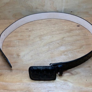 Op de afbeelding: Een zwarte leren riem met een struisvogelhuidpatroon en een bijpassende gesp.