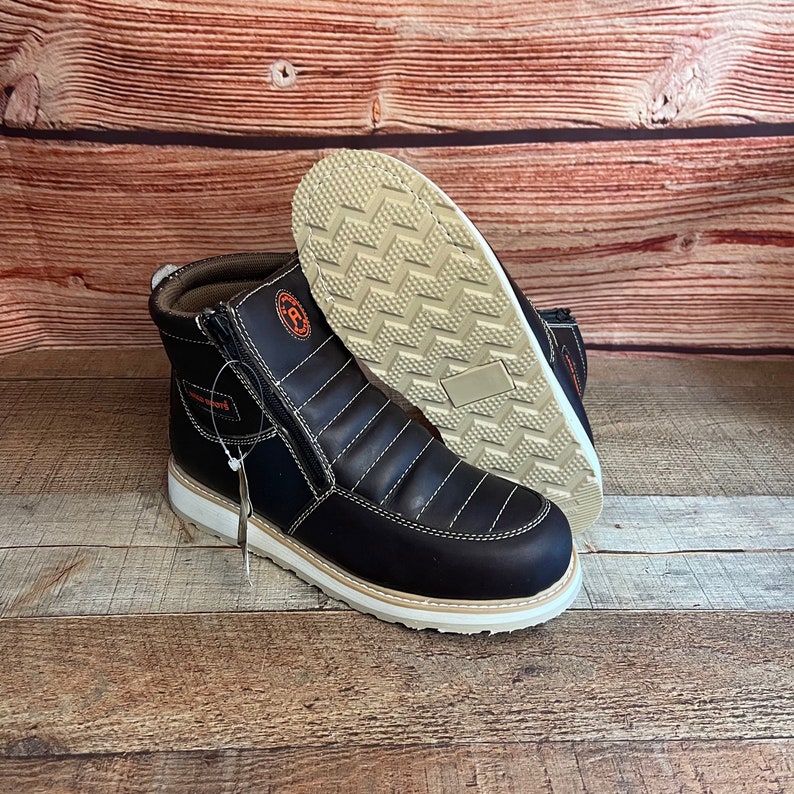 May include: A pair of black leather boots with a zipper on the side. The boots have a white sole and a brown leather upper. The boots are on a wooden surface.