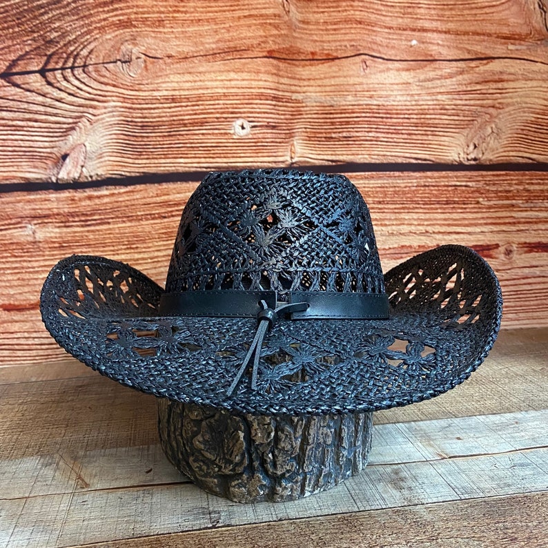 May include: A black woven straw cowboy hat with a leather band and a braided leather tie. The hat has a decorative cut-out pattern.