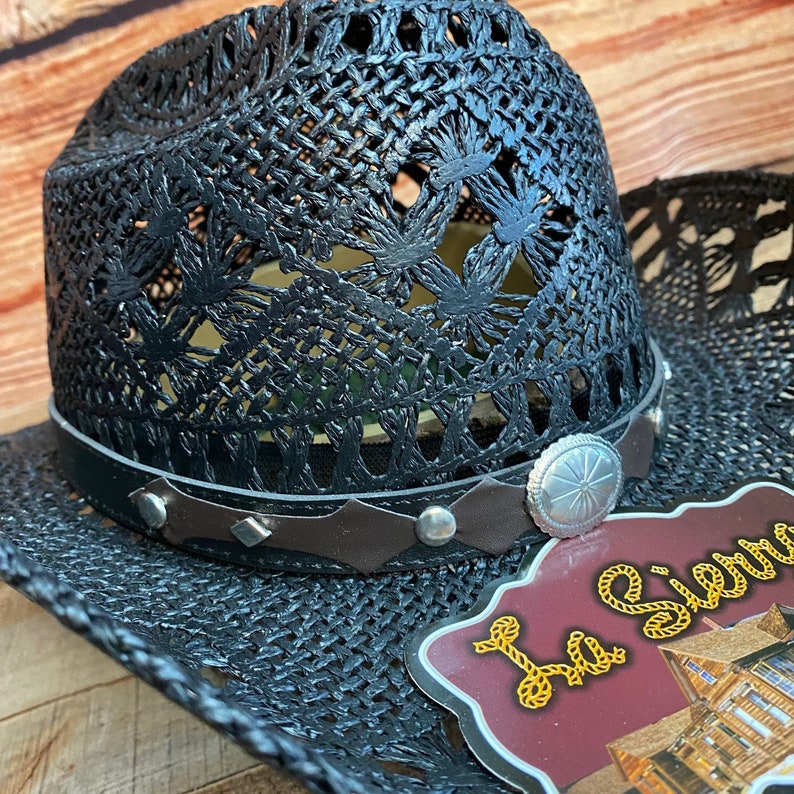 May include: Black cowboy hat with a woven design and a brown leather band with silver accents. The hat has a label that says "La Sierra".