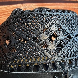 May include: Black woven straw hat with a wide brim and a black leather band. The hat has a unique design with a woven pattern and openwork details.