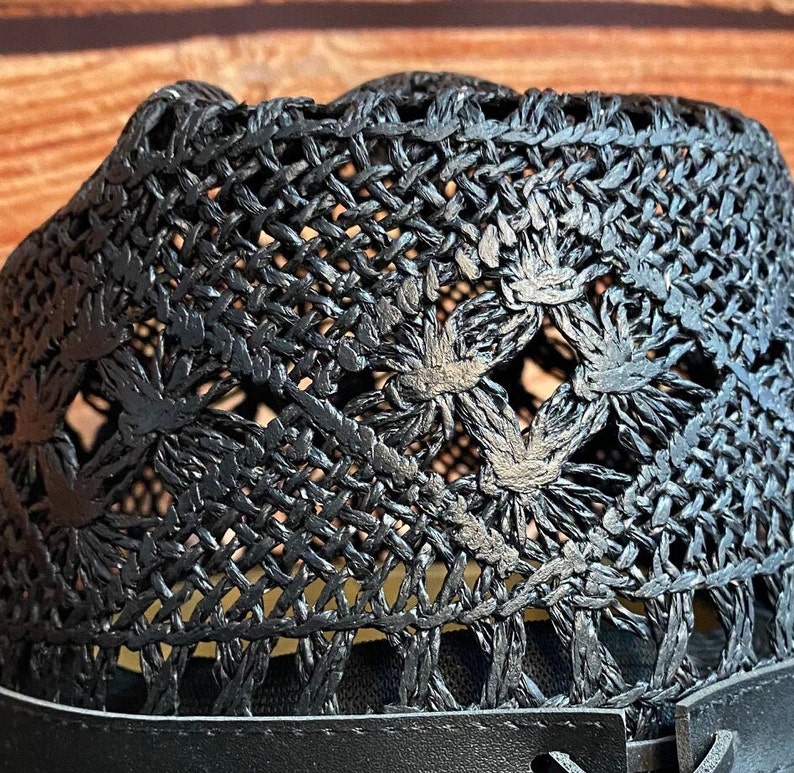 May include: Black woven straw hat with a wide brim and a black leather band. The hat has a unique design with a woven pattern and openwork details.