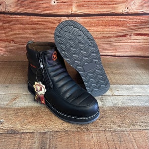May include: Black leather boots with a zipper up the front. The boots have a quilted design and a white stitching detail around the sole. The boots are on a wooden surface.
