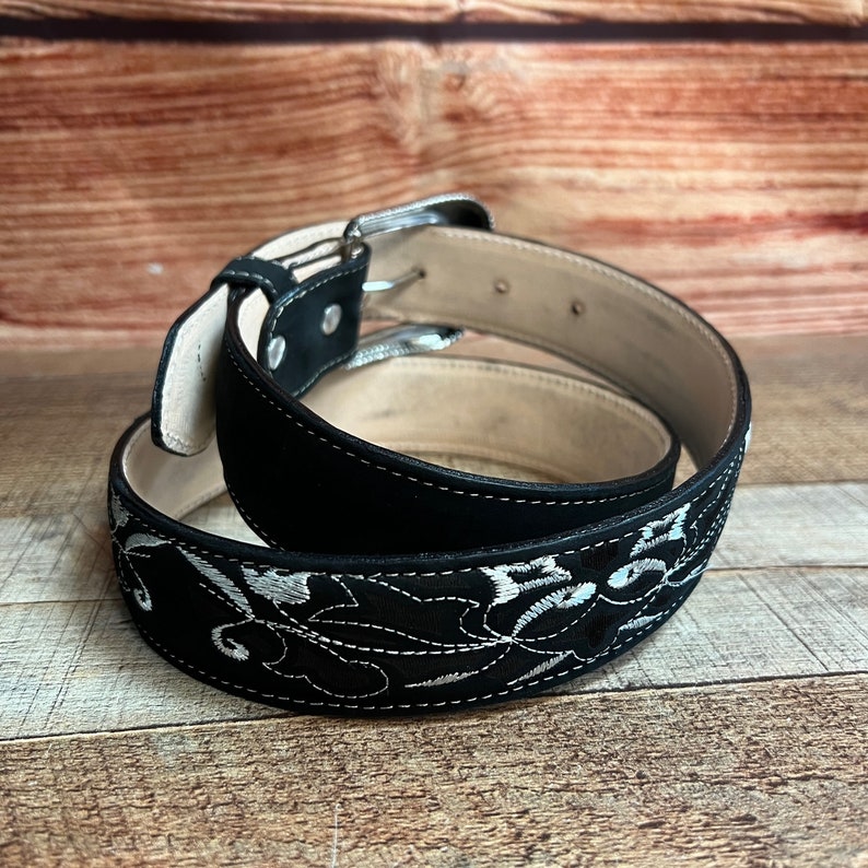 May include: A black leather belt with a silver buckle and white floral embroidery.