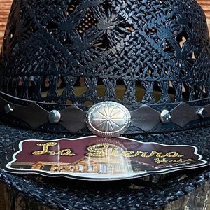 May include: Black woven straw hat with a brown leather band and a silver concho. The hat has a label that says "La Sierra Hats Since 2003".