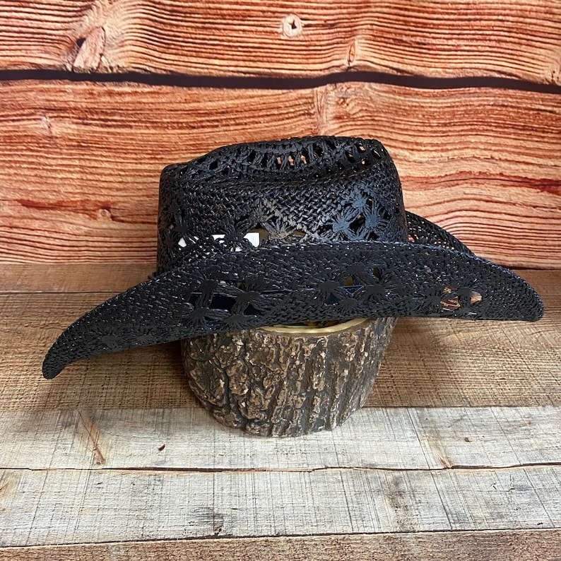 May include: A black cowboy hat with a wide brim and a lace design. The hat is made of straw and has a slightly distressed look.