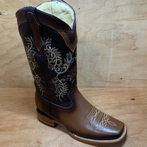 Op de afbeelding: Bruine leren cowboylaarzen met bloemenborduurwerk. De laarzen hebben een vierkante neus en een lage hak.
