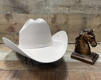 Könnte beinhalten: Ein hellgrauer Cowboyhut aus Filz mit breiter Krempe. Der Hut liegt auf einer Holzoberfläche.