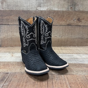 May include: Black leather cowboy boots with a snakeskin pattern and a side zipper. The boots have a white stitching detail around the top of the boot and a white sole.