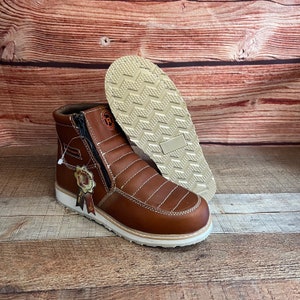 May include: Brown leather work boots with a zipper on the side and a white sole. The boots have a stitched design and a small tag with a logo on the side.