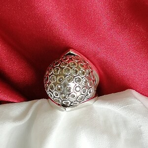 May include: A silver ring with a round, textured design. The ring is set with small, clear stones.