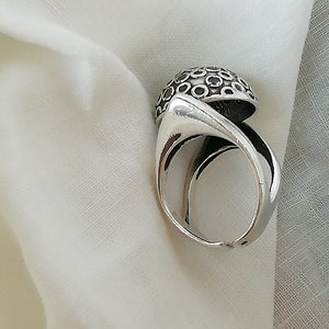 May include: A silver ring with a unique design featuring a dome-shaped top with a pattern of small circles. The ring is made of metal and has a smooth finish.
