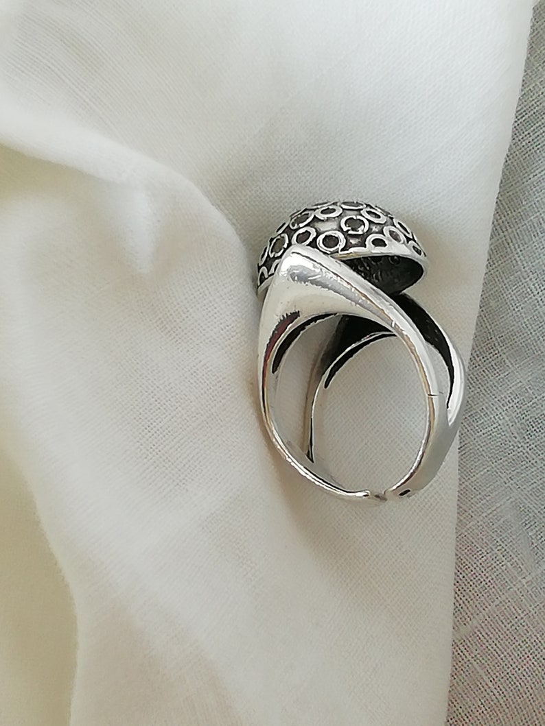 May include: A silver ring with a unique design featuring a dome-shaped top with a pattern of small circles. The ring is made of metal and has a smooth finish.