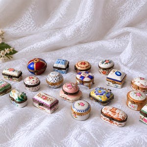 Puede incluir: Una colección de pequeñas cajas de porcelana con bisagras en varias formas, incluyendo redondas, ovaladas y rectangulares. Cada caja presenta intrincados patrones florales pintados a mano, diseños geométricos o colores sólidos con bordes de metal.
