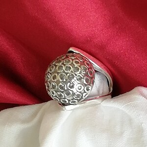 May include: A silver ring with a textured, round design. The ring is made of metal and has a unique, geometric pattern.