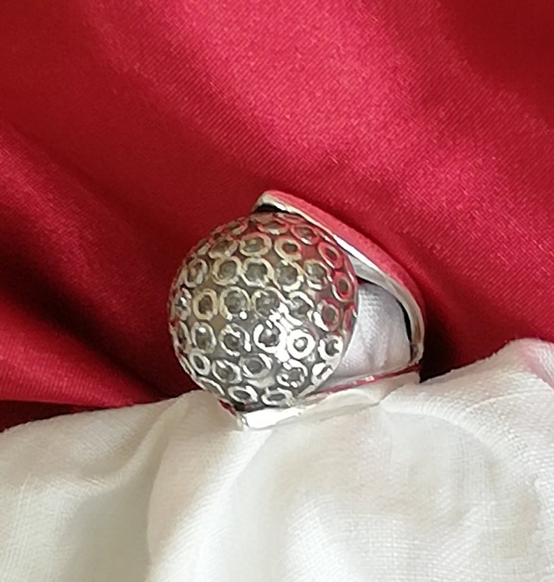 May include: A silver ring with a textured, round design. The ring is made of metal and has a unique, geometric pattern.