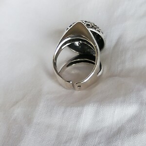 May include: A silver ring with a textured, circular design. The ring is open on one side and has a pointed tip on the other side.