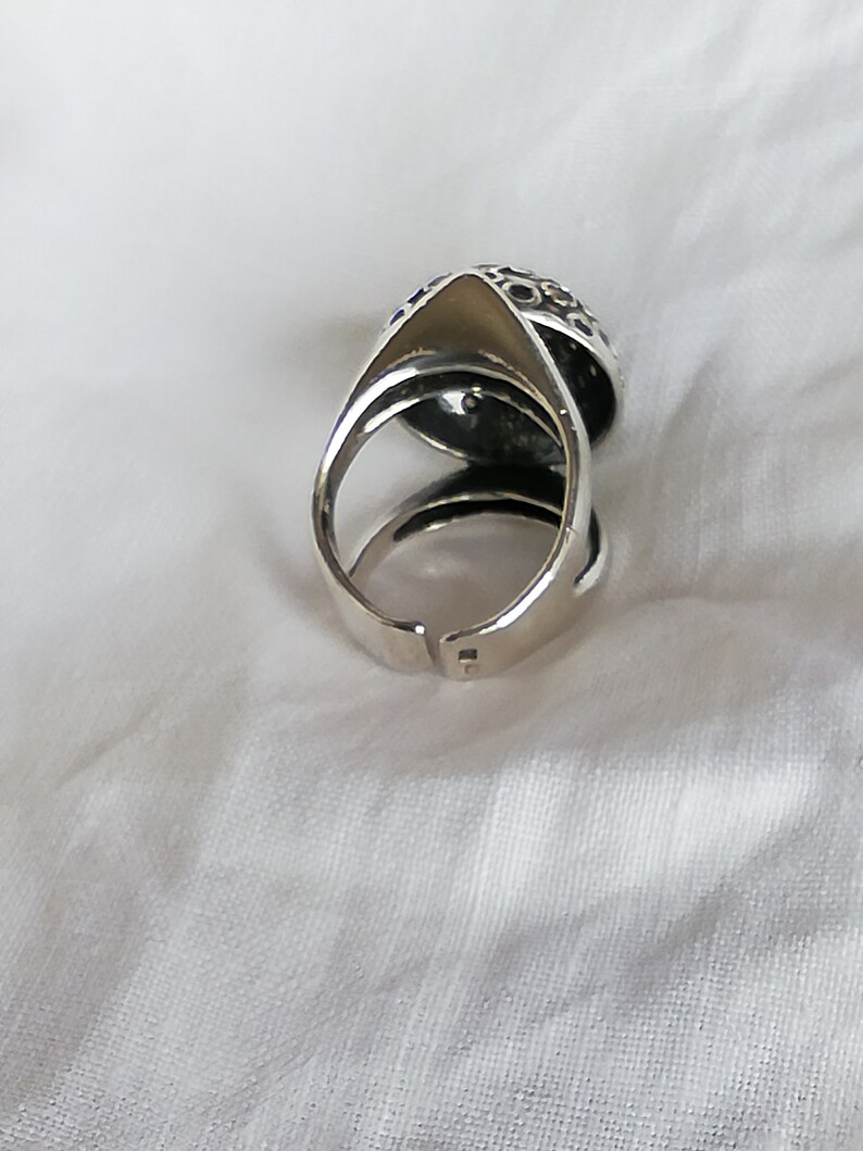 May include: A silver ring with a textured, circular design. The ring is open on one side and has a pointed tip on the other side.