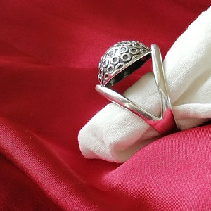May include: A silver ring with a domed top featuring a repeating circle pattern. The ring is displayed on a white fabric background.