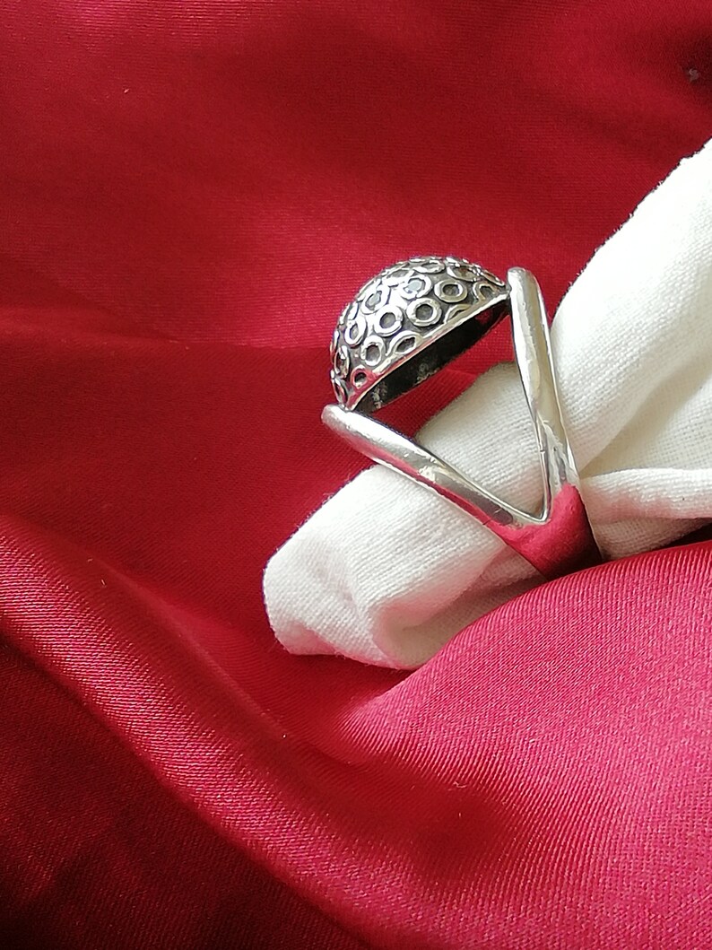 May include: A silver ring with a domed top featuring a repeating circle pattern. The ring is displayed on a white fabric background.