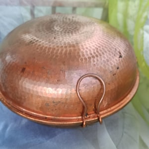 May include: A large, round copper pot with two handles. The pot has a hammered finish and is made of thick copper.