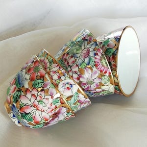 Op de afbeelding: Vier porseleinen kommen met een bloemenpatroon in tinten roze, blauw, groen en goud. De kommen zijn op elkaar gestapeld.