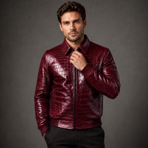 May include: A deep burgundy jacket featuring a glossy, embossed crocodile skin texture. The garment includes a classic collar, a central front zipper closure, and ribbed knit cuffs and hem. The material has a reflective, polished finish.