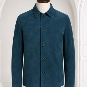 May include: A teal blue suede jacket featuring a classic point collar, long sleeves with buttoned cuffs, and a front button placket with five dark brown buttons. The garment has a horizontal seam across the chest and two side pockets.