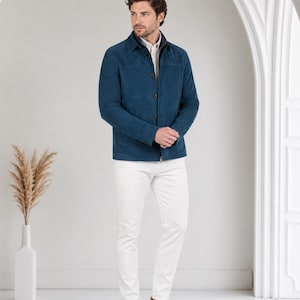 May include: A dark blue button-down jacket with a collar, worn over a light-colored shirt, paired with white trousers and beige sneakers. The jacket features a smooth texture, long sleeves, and a straight hemline, creating a clean, layered look.