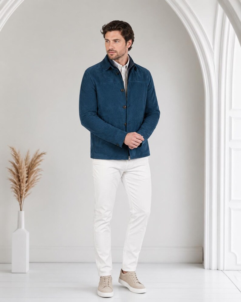 May include: A dark blue button-down jacket with a collar, worn over a light-colored shirt, paired with white trousers and beige sneakers. The jacket features a smooth texture, long sleeves, and a straight hemline, creating a clean, layered look.