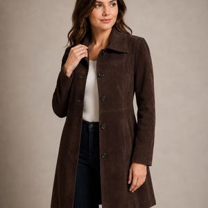 May include: A dark brown suede coat featuring a classic collar, long sleeves, and a front button closure. The coat has a structured fit with a straight hemline that falls to the mid-thigh, showcasing a smooth, matte texture throughout the garment.