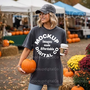 May include: A woman wearing a dark gray t-shirt, a baseball cap, and holding a pumpkin and a coffee cup. The t-shirt has a white circular graphic with the words "MOCKUP Images made Affordable DIGITAL Co."