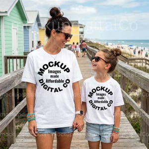 May include: A woman and a child wearing white t-shirts with the text "MOCKUP Images made Affordable DIGITAL Co" in a circular design. They are holding hands and walking on a wooden boardwalk near the beach. Both are wearing sunglasses.