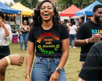 May include: A woman wearing a black t-shirt with the text "MOCKUP DIGITAL CO Images made Affordable" in a colorful design. She is wearing blue jeans and a smartwatch. The photo was taken outdoors at an event.