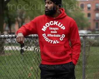 May include: A red hooded sweatshirt with a white circular graphic that reads "MOCKUP Images made Affordable DIGITAL CO". The person is wearing a black beanie and black pants. The person is leaning on a chain-link fence.