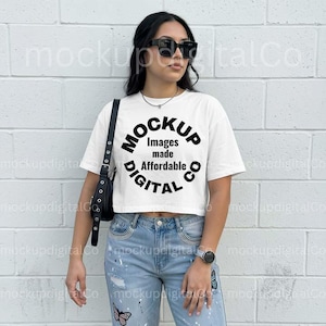 May include: A white crop top with the text "Mockup Images made Affordable DIGITAL" in a circular design. The model is wearing light blue jeans with butterfly graphics and a black shoulder bag.