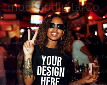 Op de afbeelding: Een vrouw met een zonnebril en een zwart T-shirt met de tekst "YOUR DESIGN HERE" erop gedrukt. Ze houdt een glas bier vast en geeft een peace-teken.