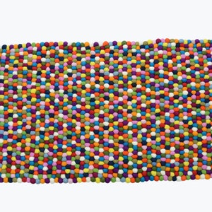 May include: A colourful rug made of felt balls in various shades of red, orange, yellow, green, blue, purple, pink, and white. The balls are arranged in a close-knit pattern, creating a textured and visually appealing surface.