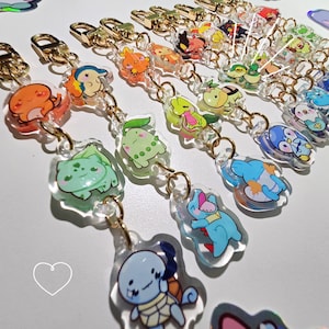May include: A collection of colourful, clear acrylic keychains featuring cartoon characters. Each keychain has a gold metal ring and a clear acrylic chain.
