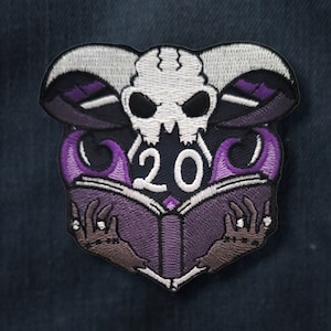 Op de afbeelding: Paarse en witte geborduurde patch met een schedel, vlammen en een boek met het nummer 20 erop.