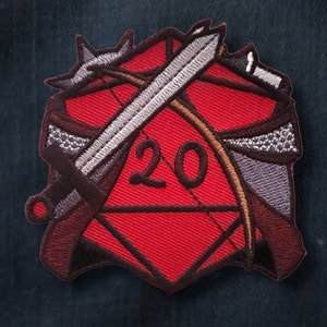 Peut inclure: Un dé rouge à 20 faces avec une épée et un arc et une flèche croisés dessus. Le dé est entouré de coutures noires et l'épée, l'arc et la flèche sont brodés en gris et marron.