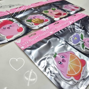 Peut inclure: Un ensemble de six diffuseurs de parfum de voiture roses et blancs représentant un personnage de dessin animé rose avec différents motifs de fruits. Les diffuseurs sont emballés dans des sachets en plastique transparent avec un emballage rose et blanc qui dit "Cute House Crafts Cute House Crafts".