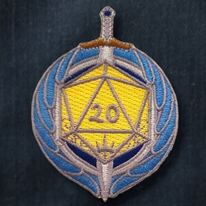 May include: A blue and silver embroidered patch featuring a 20-sided die with a sword behind it.