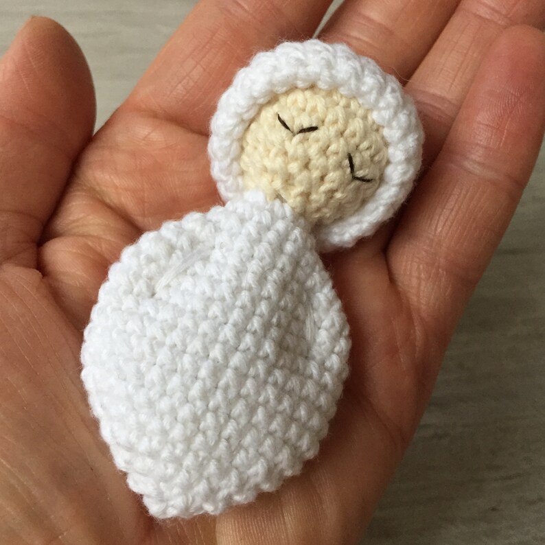 May include: A white crocheted baby doll with closed eyes, wearing a white crocheted hat.