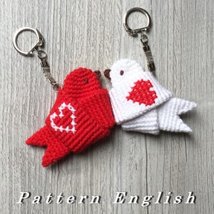 Op de afbeelding: Twee gebreide vogel sleutelhangers, een rood en een wit, met een wit hart op de rode vogel en een rood hart op de witte vogel. De sleutelhangers zijn bevestigd aan zilveren sleutelringen.