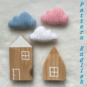 May include: Three crocheted clouds in pink, blue, and white, and two wooden houses with white painted doors and windows. The text "Pattern English" is written vertically on the right side of the image.