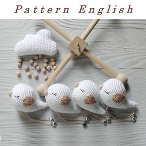 Op de afbeelding: Een witte gehaakte wolkenmobiel met vier witte gehaakte vogels met bruine snavels en ogen. De mobiel heeft houten stokjes en houten kralen.